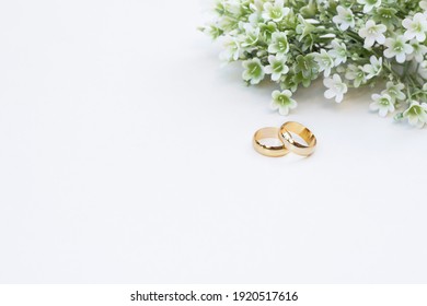 White and green flowers and two golden wedding rings on white background.