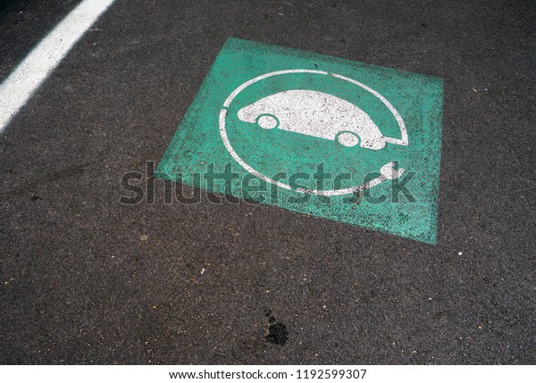 White and green symbol of electric car charging,\
on asphalt