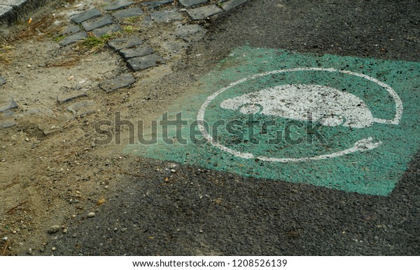 White and green symbol of electric car charging,\
on asphalt