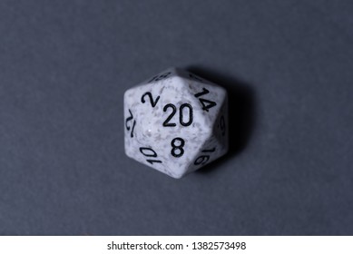 White, grey, and black 20-sided die (d20, also an icosahedron) on a grey paper background. This is part of a dice set commonly used for pen and paper tabletop role playing games (RPGs).