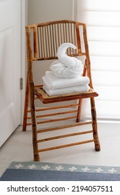 White Guest Bath Towel Folded In Fancy Style In Shape Of Swan Sitting Atop Stack Of Towels On Chair In Bed And Breakfast Hotel Bathroom