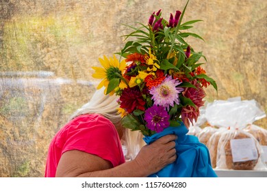 White Haired Woman Shops For Bread With Face Obscured By A Huge Boquet Of Beautiful Colorful Flowers With Blurred Background