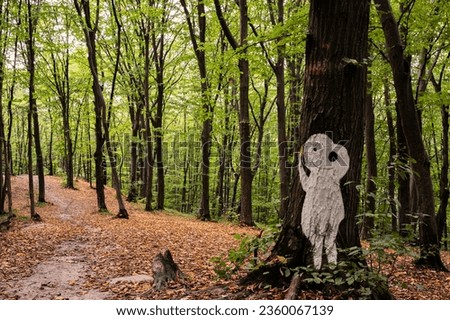 White halloween silhuette of man or alien pictured on tree in forest, covered with yellow dry leafs, with another such silhuettes on background. Scenic, beautiful, mistic, postcard view, wallpaper