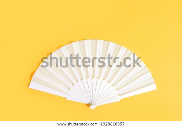 White hand fan on\
yellow background, top\
view