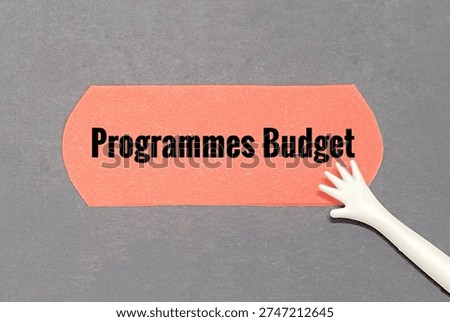 White hand model pointing at orange paper written programmes budget as financial plan that allocates resources to specific activities, goals, or projects rather than traditional line-item expenses like salaries or supplies