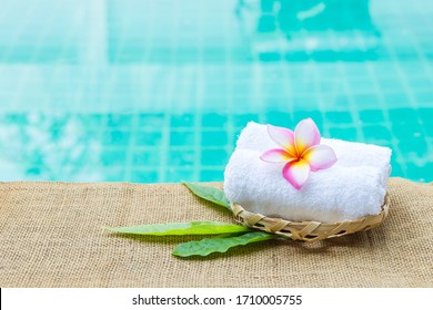 White Hand Towel With Beautiful Plumeria Flower In Bamboo Basket Witth Space On Blue Water Background, Spa And Wellness Concept Background, Outdoor Day Light