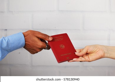 White hands and black hands holding a german passport in front of a white brick wall