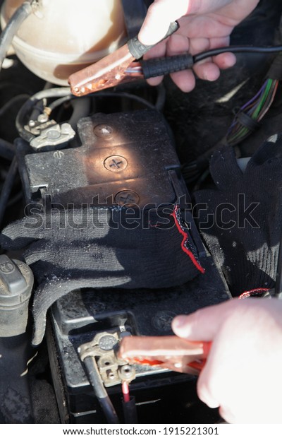 The white hands\
connects the starting wires terminals on frozen car engine, cold\
start with spare battery accumulator and power wires with crocodile\
clips at Sunny winter day
