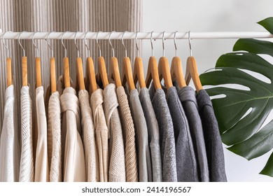 White hanger with beautiful clothes in neutral colors. Monstera flower with large leaves. White background.