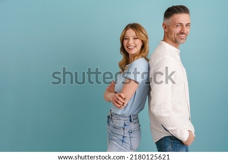 White happy man and woman smiling while standing back to back isolated over blue background