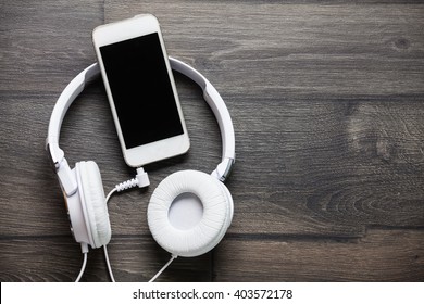White headphones and smart phone on wooden table