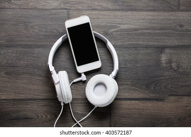 White Headphones And Smart Phone On Wooden Table