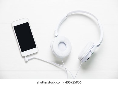 White Headphones And Smart Phone On White Wooden Table