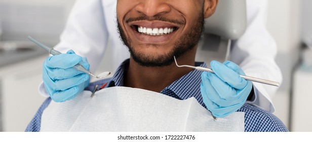 White healthy black male smile and dentist hands with instruments, panorama, cropped