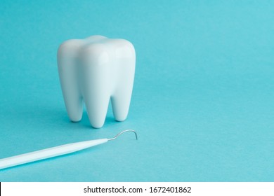 White healthy tooth model and dental pick explorer probe on blue background with copy space. Dental care and healthcare concept.