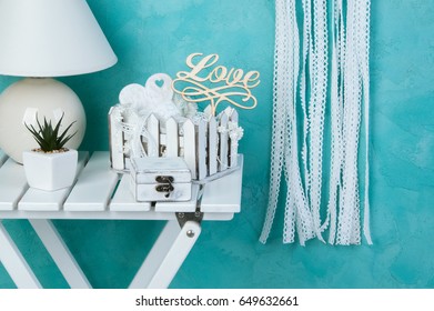 White heart lace dream catcher with crochet flowers, white nightstand , shabby wooden casket , wooden heart and shabby basket with lace  on aquamarine textured background. Texture of concrete