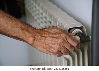 White heating radiator hanging on white wall, close up view. Person turns on or turns off radiator. Heating is getting more expensive, save money. Energy crisis.