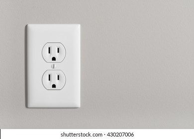 A white home electrical outlet on a light grey wall.