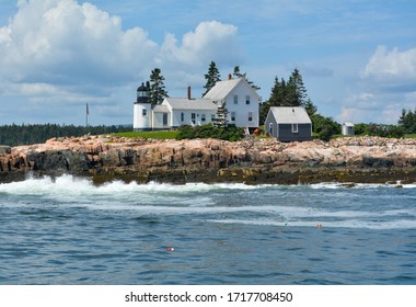 White Home On An Island In Bar Harbor, Maine With Small Lighthouse, Rocky Coast, Blue Ocean And USA Flag