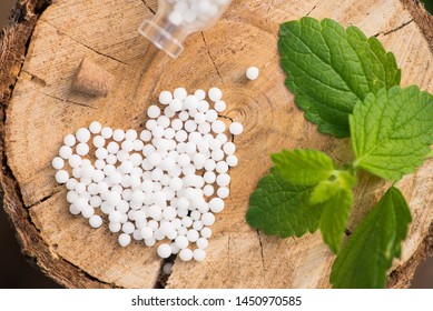 White homeopathic globules  in the form of a heart and green leaf mint in a wood stump. Treatment by alternative methods. Healthy lifestyle. Top view.