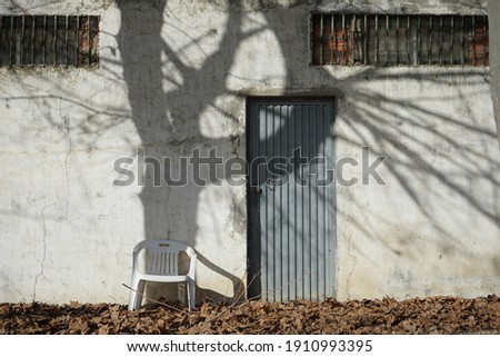 white house facade with blue door and chair and tree shadow