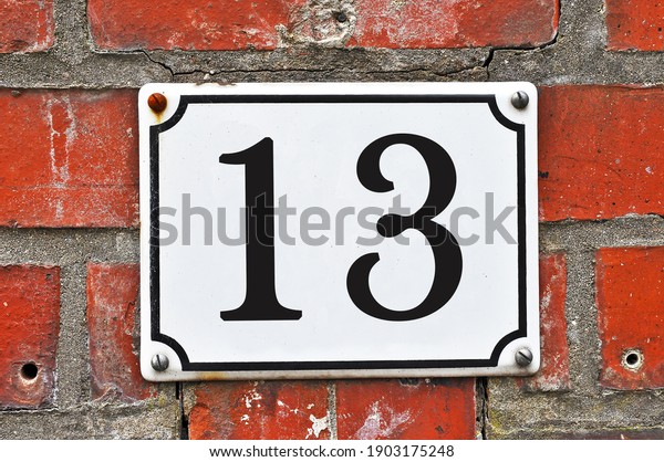 A white house number plaque, showing the number\
thirteen (13)