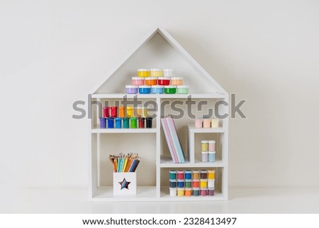 White house shaped shelving with various material for creativity and kids art activity. Stationery and supplies for drawing and craft. Organizing and storage in craft room.