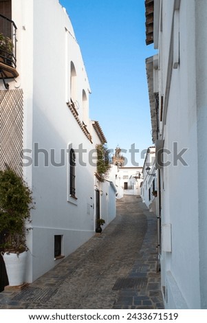 White houses on the whitewashed streets of a small Andalusian town. The narrow Fria Street in Sanlucar de Guadiana. The bell tower of Our Lady of the Flowers church at the background. Spain. 2019.