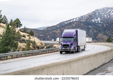 White industrial big rig long hauler semi truck tractor with grille guard and dry van semi trailer transporting commercial cargo running on the winding highway road with mountain pass in California