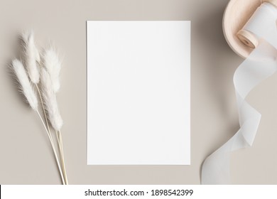 White invitation card mockup with a lagurus on a beige table. 5x7 ratio, similar to A6, A5.