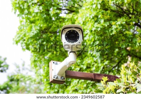 White IP CCTV surveillance camera against green tree foliage. Concept of security, private territory, property control. Program searching for criminals with facial recognition. Modern technology. 