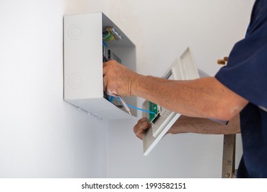 The white iron box is mounted on the wall and the wires are embedded inside the wall.
					
					Indoor electric circuit control box and a technician is installing and controlling the circuit. Construction 