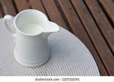 White jug with milk on a wooden table. Breakfast on the veranda. Fresh drink, autumn leaves and oudoor. Close up photography