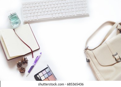 White Keyboard, Open Notebook, Perfume Bottle, Pine Cones, Purple Pen, Eyeshadow And Beige Lady's Bag. Female Desktop Top View. Flat Lay Work Space Photo