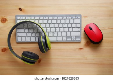 White keyboard with wireless mouse and bluetooth wireless headphones on wooden background.Top view. Computer equipment accessories