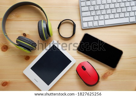 White keyboard with wireless mouse and bluetooth wireless headphones and other electronic gadgets for daily use on wooden background.Top view.