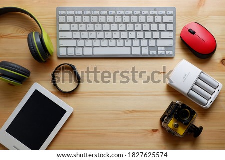 White keyboard with wireless mouse and bluetooth wireless headphones and other electronic gadgets for daily use on wooden background.Top view.