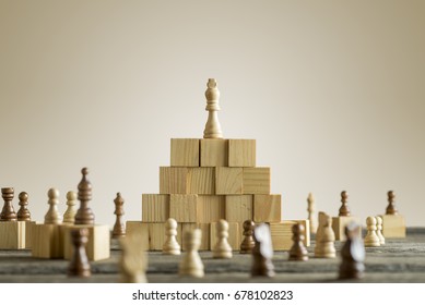 Weißer König auf Holzbausteinen mit anderen arrangierten Schachstücken unter der Pyramide.