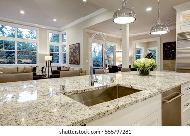 White kitchen design features large bar style kitchen island with granite countertop illuminated by modern pendant lights. Northwest, USA