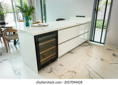 White kitchen island granite countertops and white drawer cabinet, Have modern black Built in wine refrigerator under countertop. Beautiful white marble floor tiles.