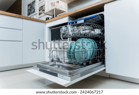 The white kitchen and opened dishwasher with clean dishes