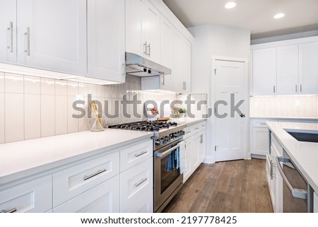 white kitchen with stools tile backsplash chefs island stainless appliances wood floor