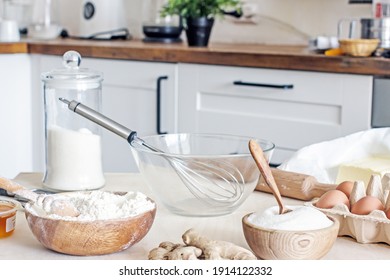 White kitchen table with ingredients and accessories for homemade baked goods. Flour, sugar, eggs, butter, honey, ginger, bowl, whisk, rolling pin. Homemade authentic hobby baking - Powered by Shutterstock