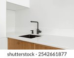 White kitchen table top, black sink with black water tap, against a white wall, horizontal with copy space