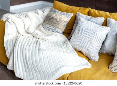 white knit blanket  on a yellow couch and nice decorative cushions 
