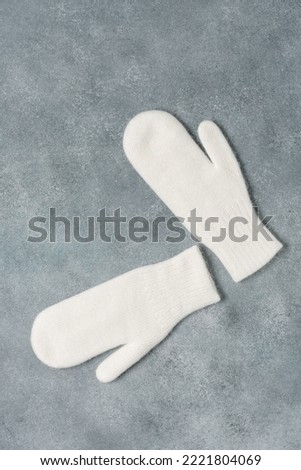White knitted mittens on a gray rustic background. Down mittens. Top view, flat lay, copy space.