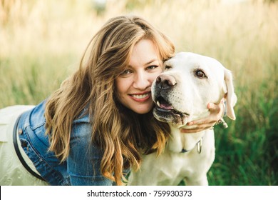 A white labrador purebred dog plays with a beautiful girl in grass and licks her face