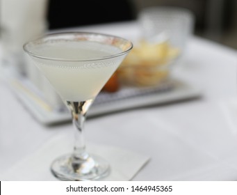 White lady gin cocktail in martini glass with crisps in the back. Very selective focus