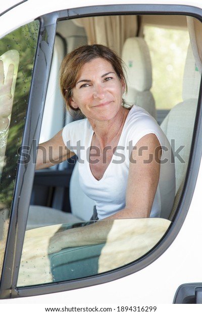 White lady in white shirt looks out\
of the window sitting behind the wheel of her\
camper