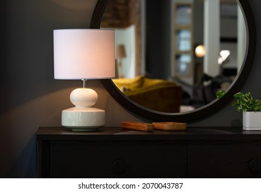 A white lampshade on a black drawer and a mirror on the wall.